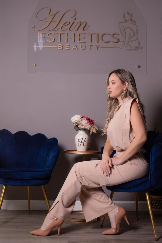 Elisangela Hein, especialista em estética avançada, sentada no ambiente sofisticado da recepção de sua clínica, a Hein Esthetics.