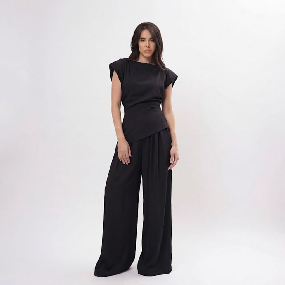 Modelo com blusa preta estruturada de manga curta e calça de perna ampla em estúdio claro