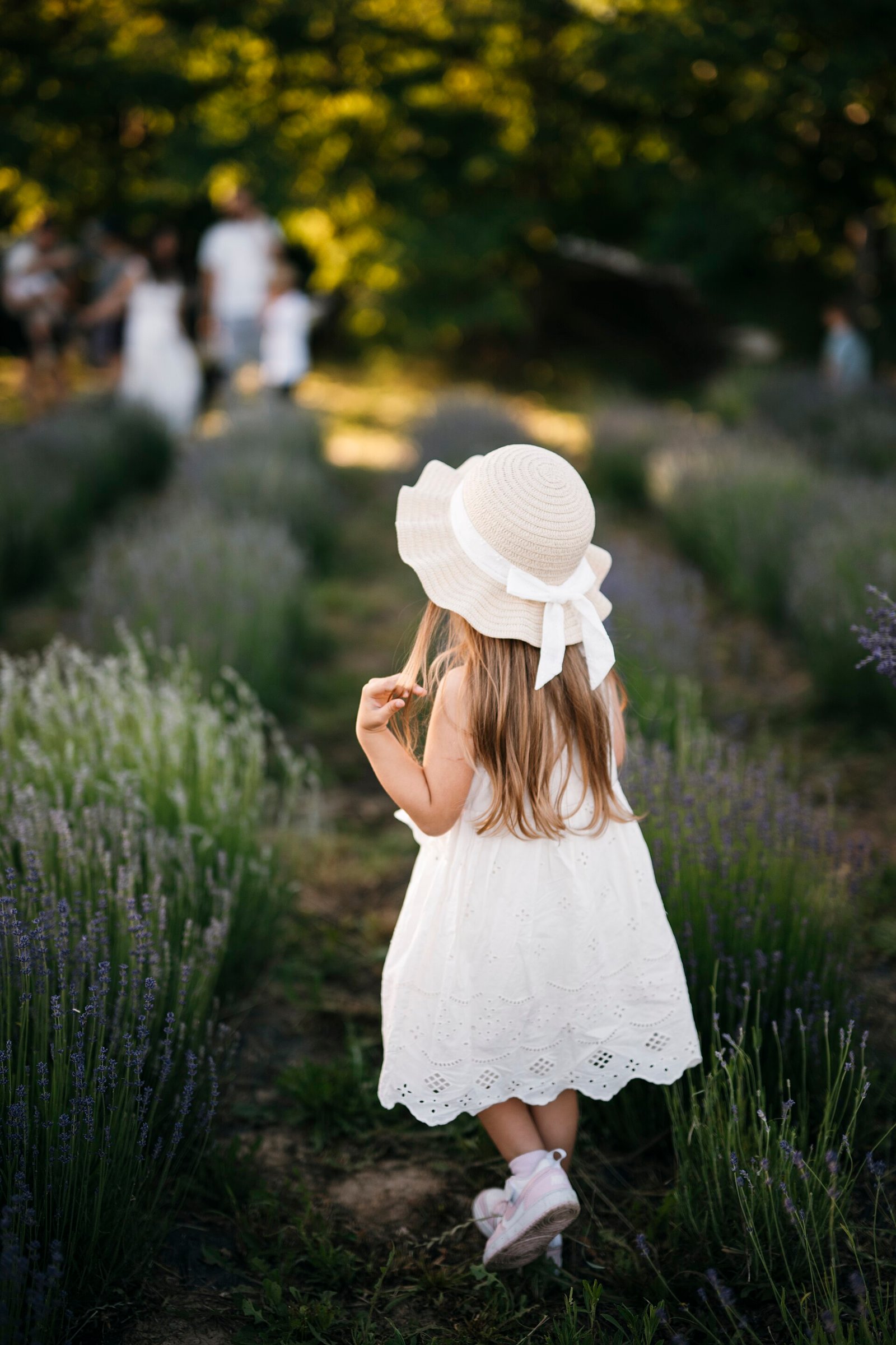 Criança caminha por campo de lavanda usando chapéu de palha de aba larga, medida física de proteção solar
