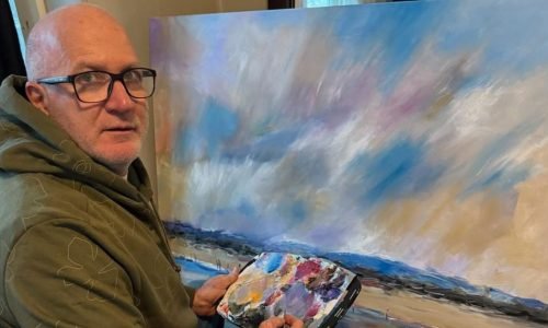 Retrato de um homem sentado en frenta a uma tela que está pintando.